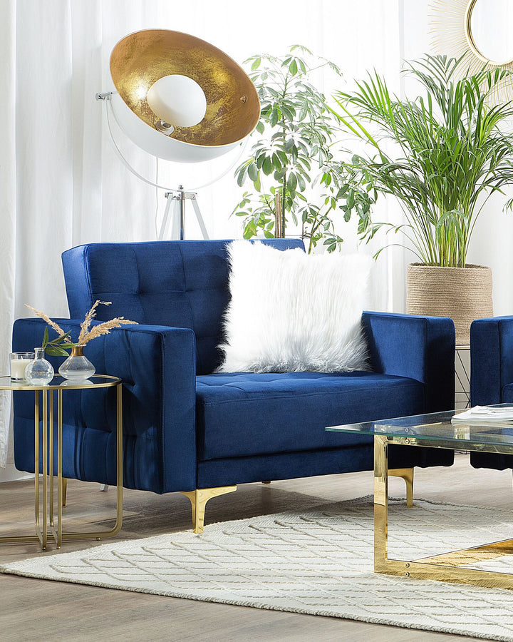 Navy blue velvet armchair with gold metal legs, featuring a tufted backrest, in a stylish living room setting.