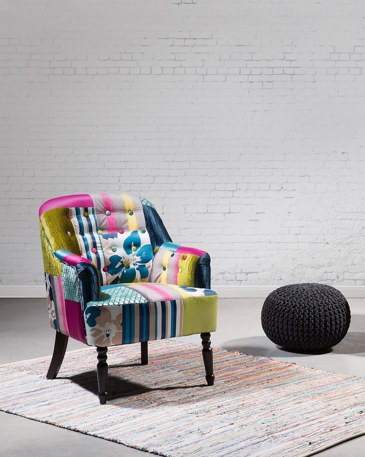 A colorful patchwork armchair with a solid wood frame and legs, upholstered in a multicolor design, positioned in a room with a patterned rug and a modern sculpture.