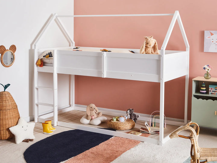 Children's room with a white house-shaped bed, toys, and a pink wall.