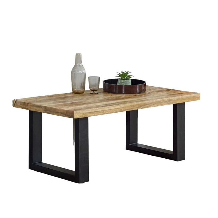 A rectangular coffee table with solid mango wood top and black metal legs, featuring a natural lacquer finish and a decorative item on top.