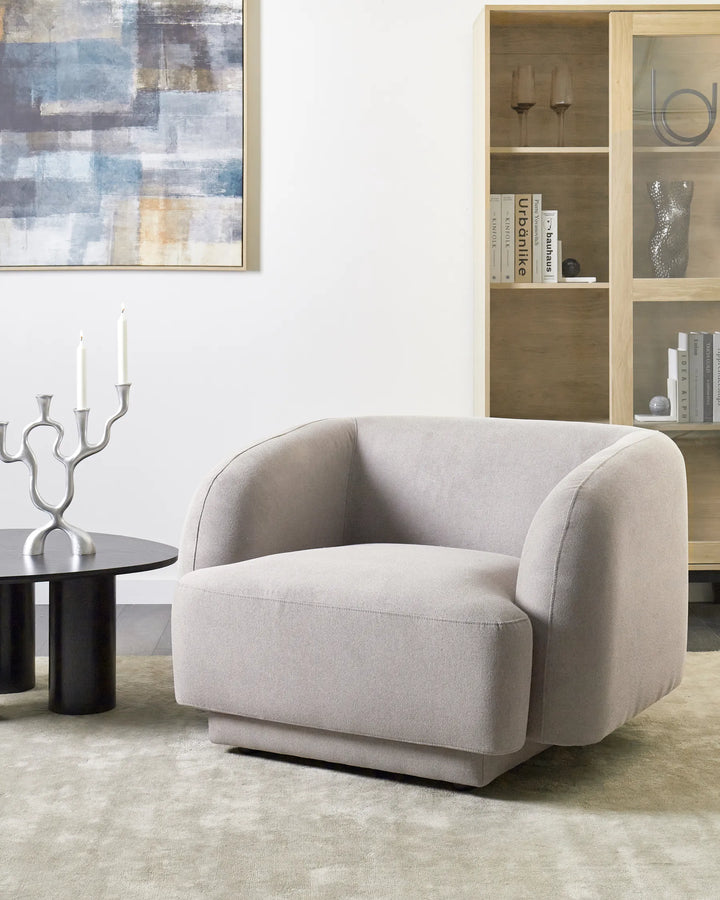 Gray armchair in a living room setting with a bookshelf and abstract painting.