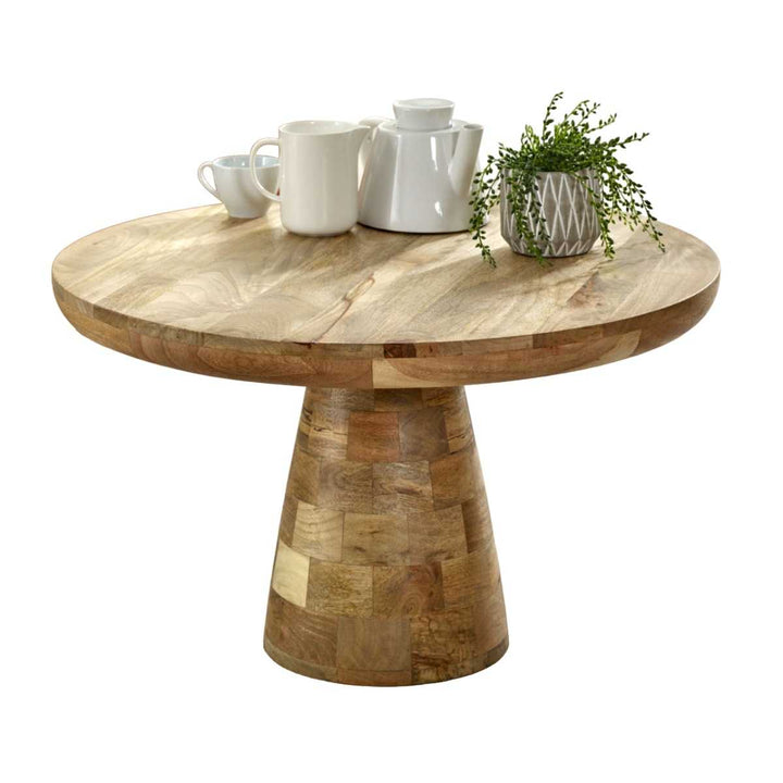 A round, solid wood coffee table with a mushroom style design, featuring a natural lacquered finish and placed on a pedestal base. The table is set with coffee cups and a decorative vase with flowers on top.