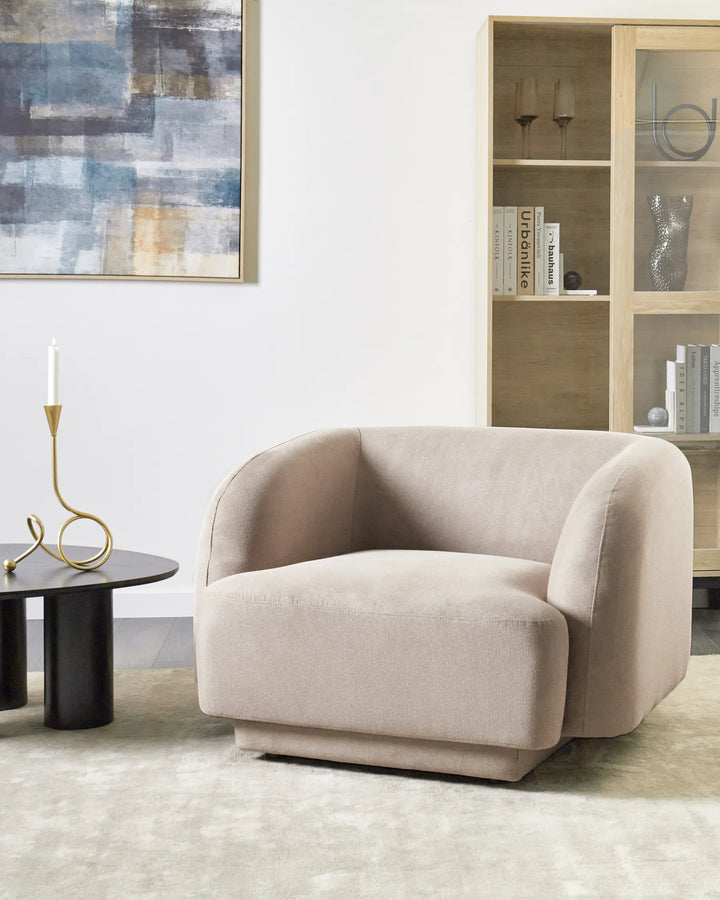 Beige armchair in a modern living room with abstract art and bookshelf.