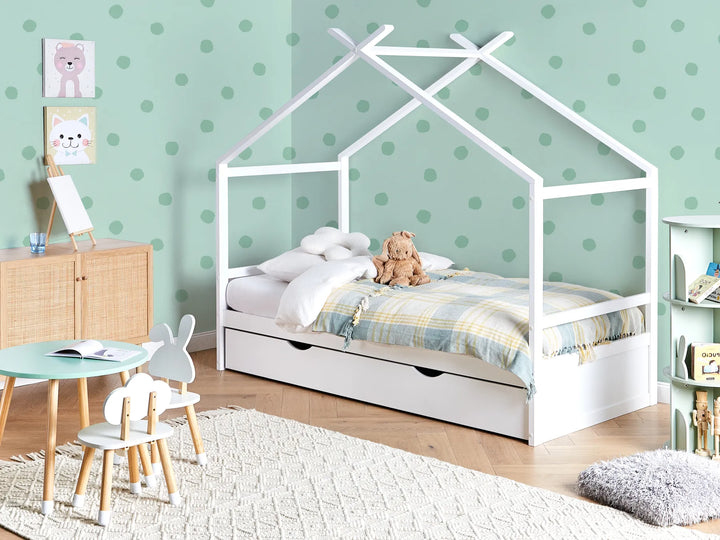 Children's room with a white house-shaped bed, teddy bear, and polka dot wallpaper.