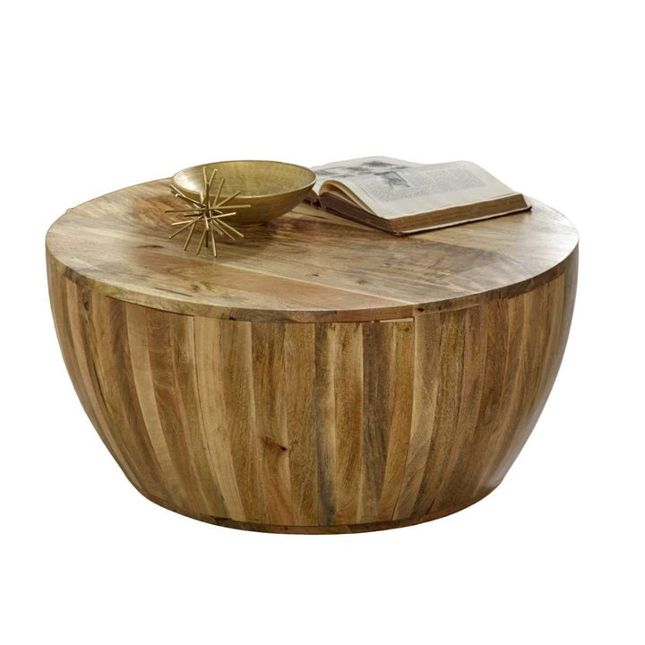 A round, solid mango wood drum-shaped coffee table with a chic design, featuring a natural finish and resting items including a book and a decorative object on its top surface.