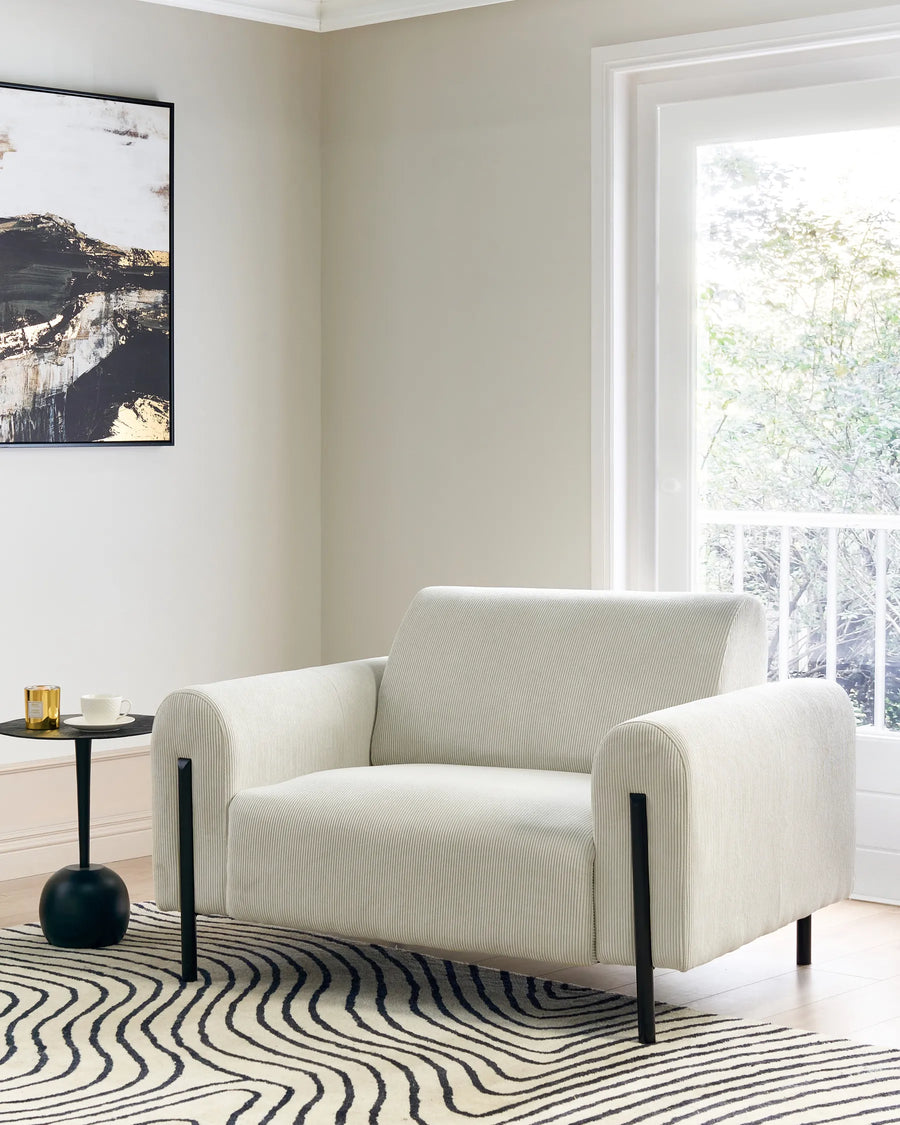 White armchair in a modern living room with a side table and artwork on the wall.