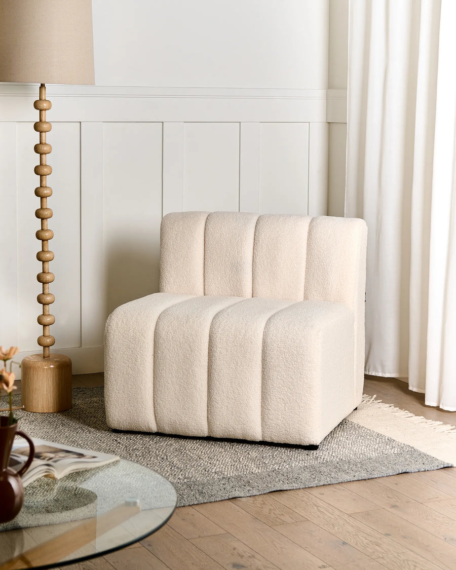 Beige armchair in a room with wooden floor, lamp, and curtains