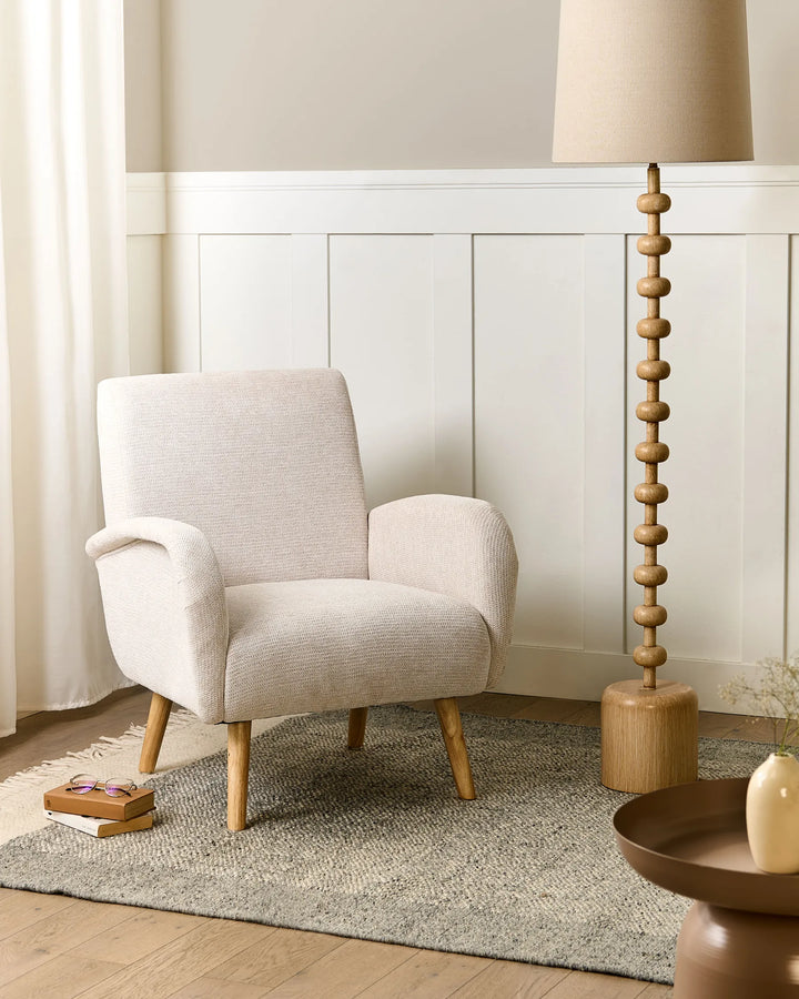 Beige armchair in a room with a lamp and decorative items on a rug.
