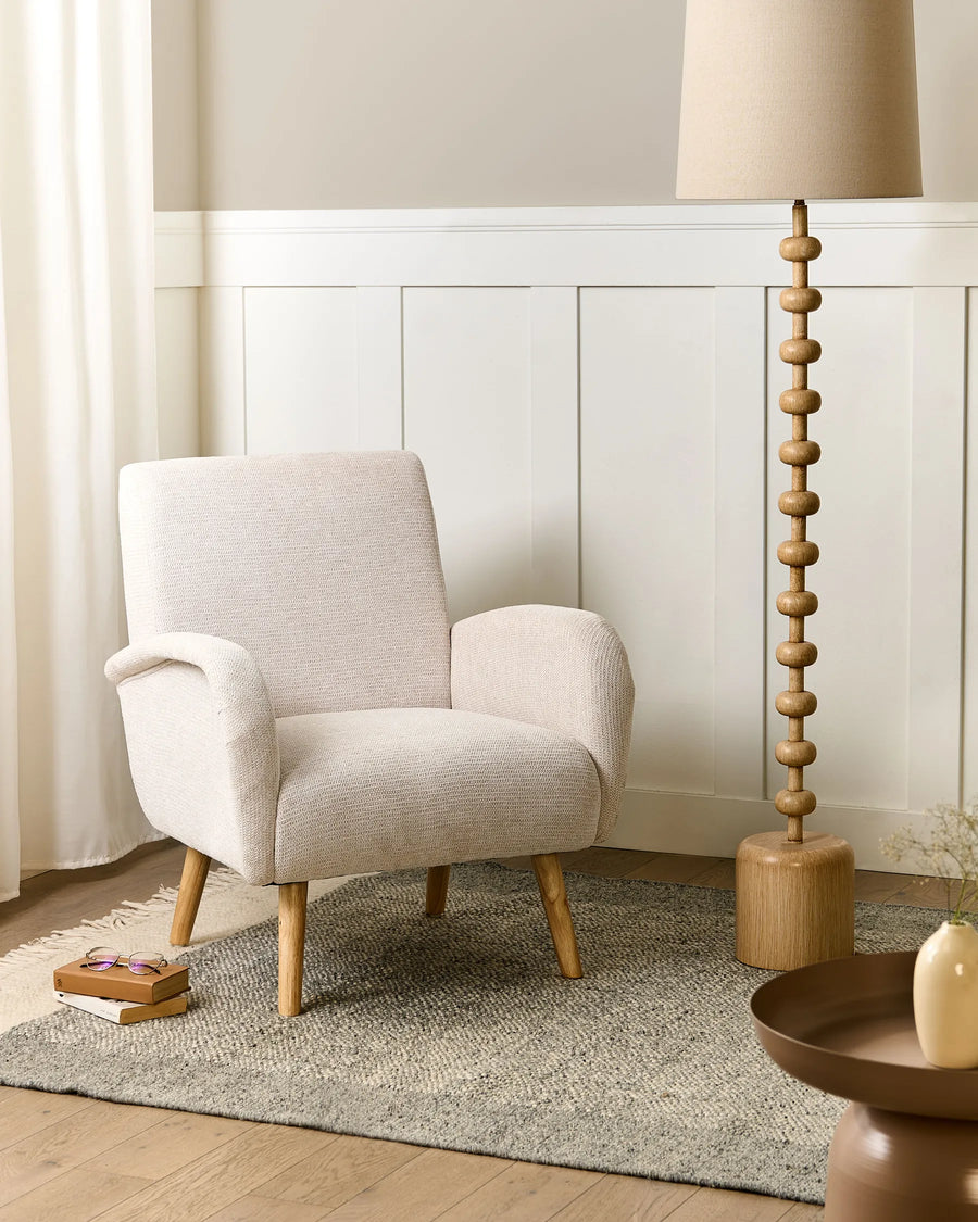 Beige armchair in a room with a lamp and decorative items on a rug.