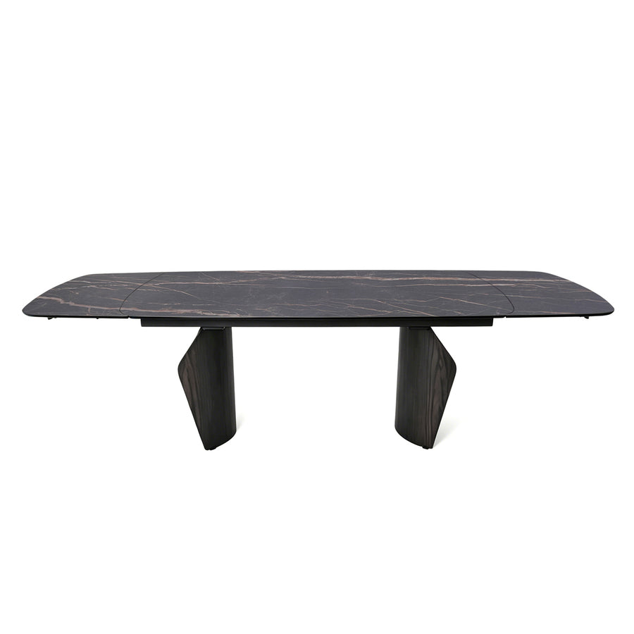 A modern rectangular dining table with a dark black marble top featuring subtle light veining, supported by two sculptural dark wood legs, shown against a plain white background.