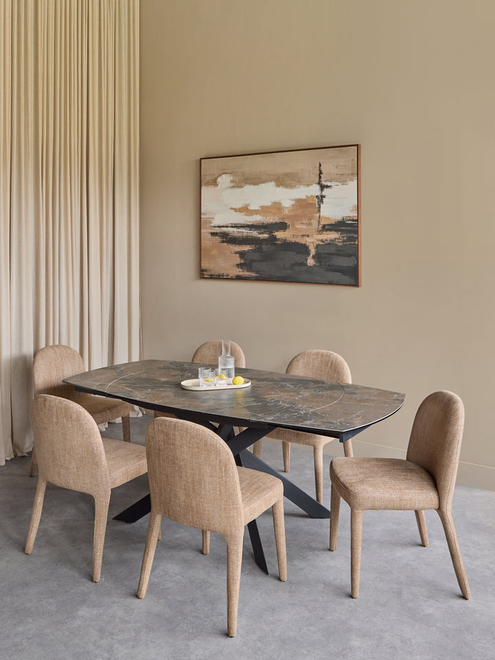 A modern dining set featuring a dark stone rectangular table with a black metal base and six upholstered dining chairs in a neutral beige tone, set in a minimalist dining room with a beige wall, abstract painting, and pleated curtains.