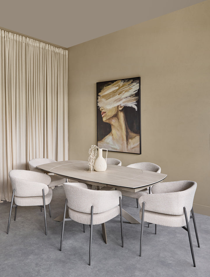 A modern dining room setup featuring a light wood oval dining table surrounded by six upholstered dining chairs in a light beige fabric with slim dark metal legs. The room has beige walls, a gray textured floor, a beige pleated curtain, and a framed abstract portrait painting hanging on the wall.