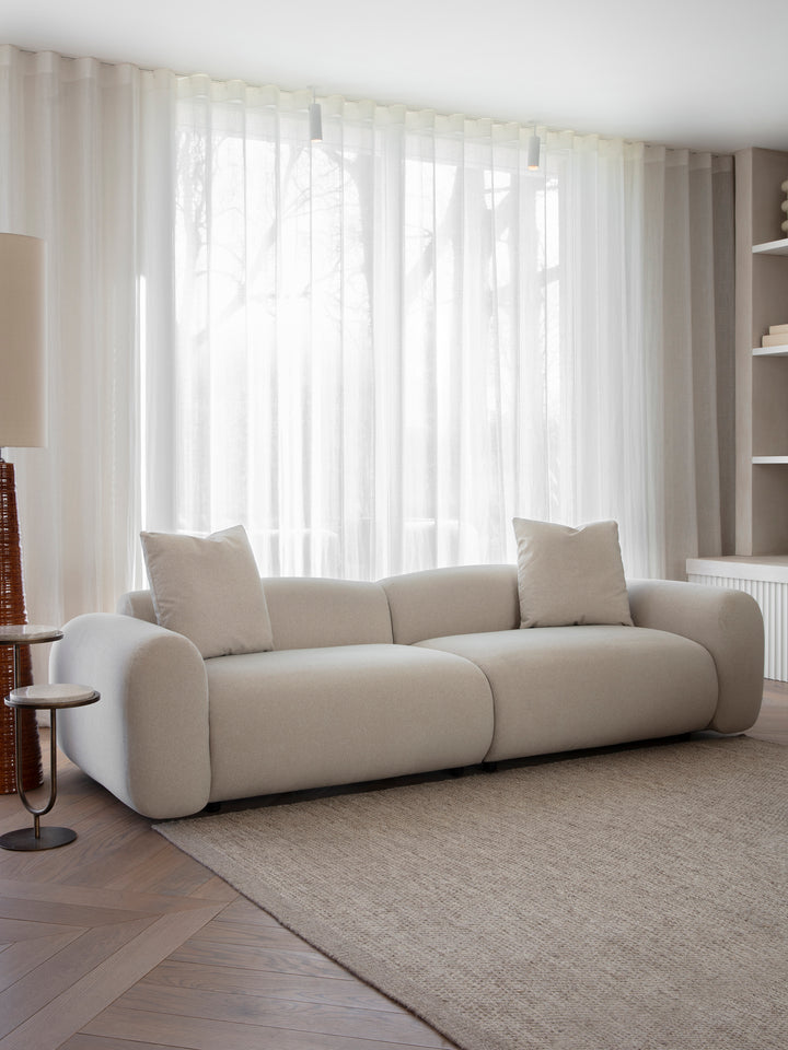 Beige sofa in a living room with large windows and curtains