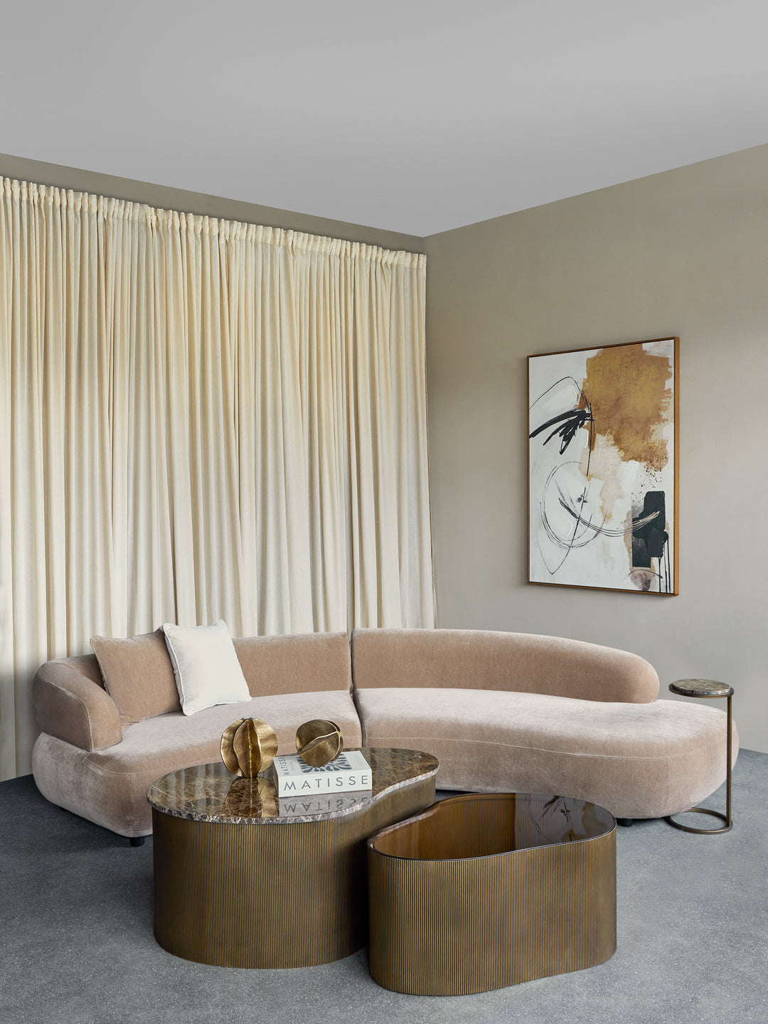 Modern living room with a curved beige sofa, gold coffee table, and abstract art on the wall.