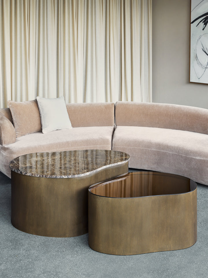 Modern living room with a curved beige sofa and a unique shaped bronze coffee table.