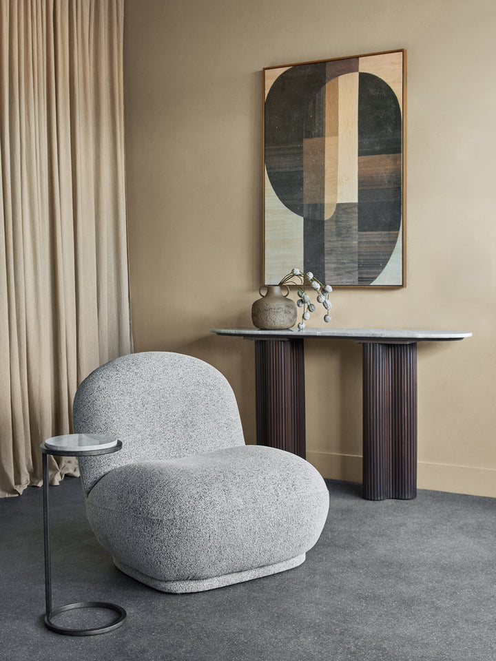 Gray armchair in a room with a abstract painting on the wall and a small table.