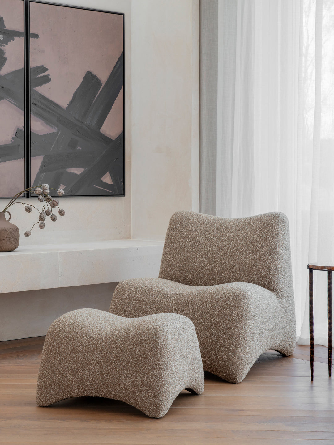 Modern beige lounge chair and ottoman in a room with abstract art and large windows.