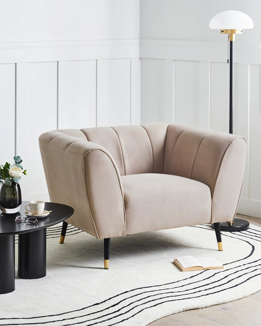 Beige armchair in a modern living room setting with a white wall and black coffee table.