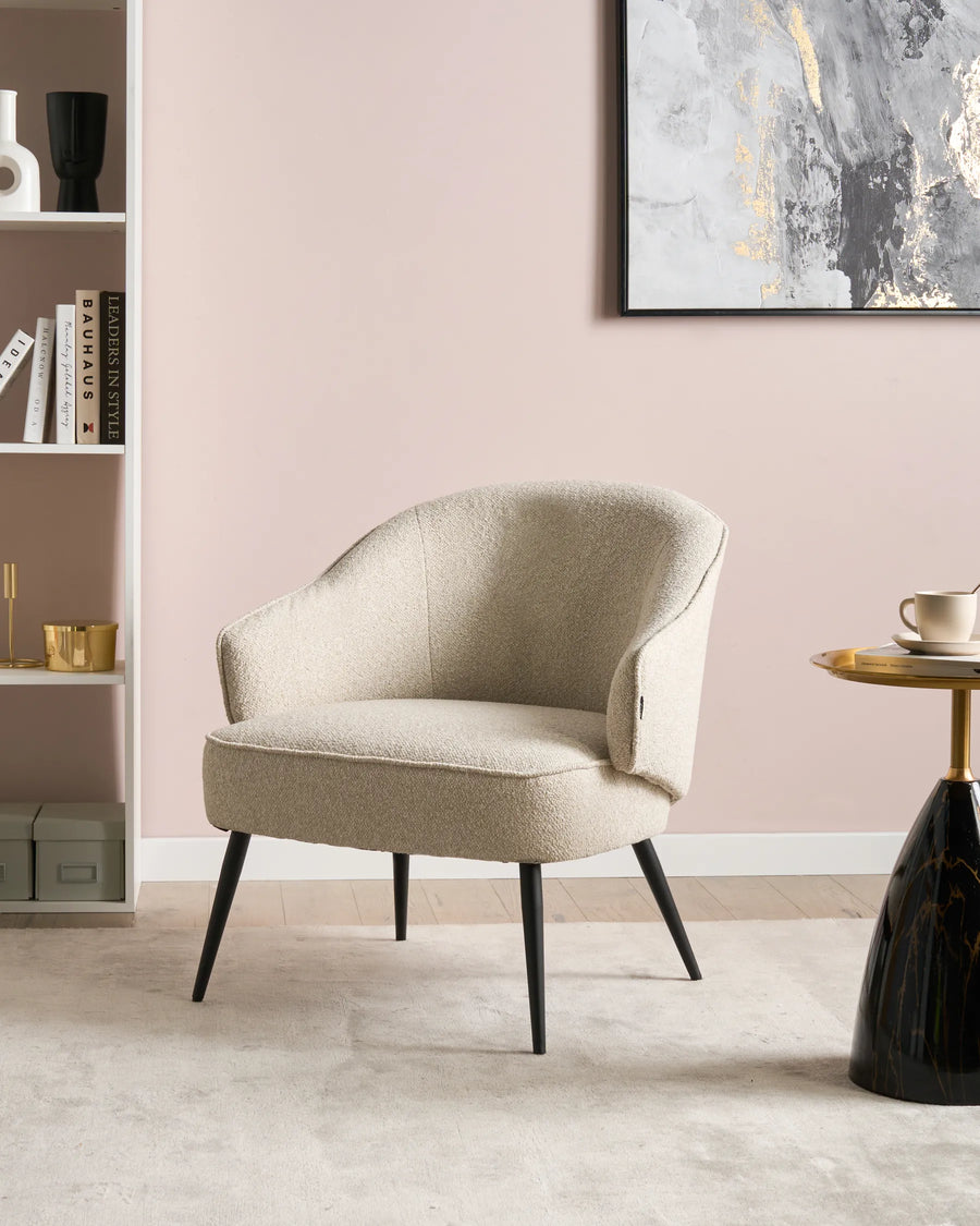Beige armchair in a room with a pink wall, bookshelf, and side table.