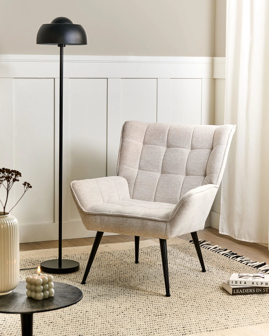 Beige armchair in a living room setting with a black floor lamp and decorative items.