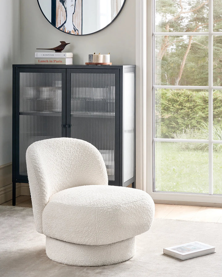 White textured armchair in a room with a black cabinet and large window