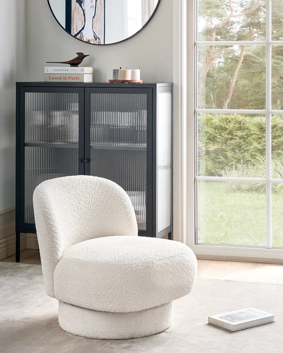 White textured armchair in a room with a black cabinet and large window