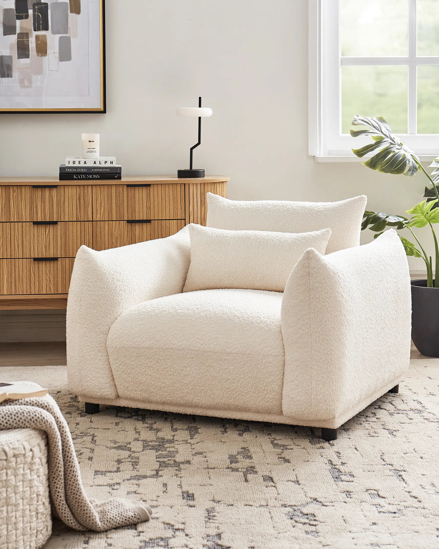 Beige armchair in a living room setting with a wooden cabinet and window in the background.