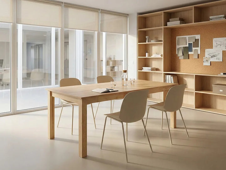 A modern dining table and four matching chairs in a minimalist, warm-toned office or dining room setting with large windows and built-in wooden shelving.