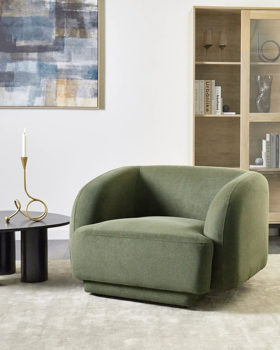 Green armchair in a living room setting with a abstract painting and bookshelf in the background.