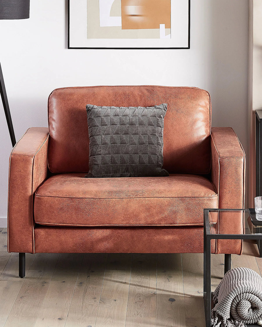 Brown leather armchair with a gray pillow in a room setting.