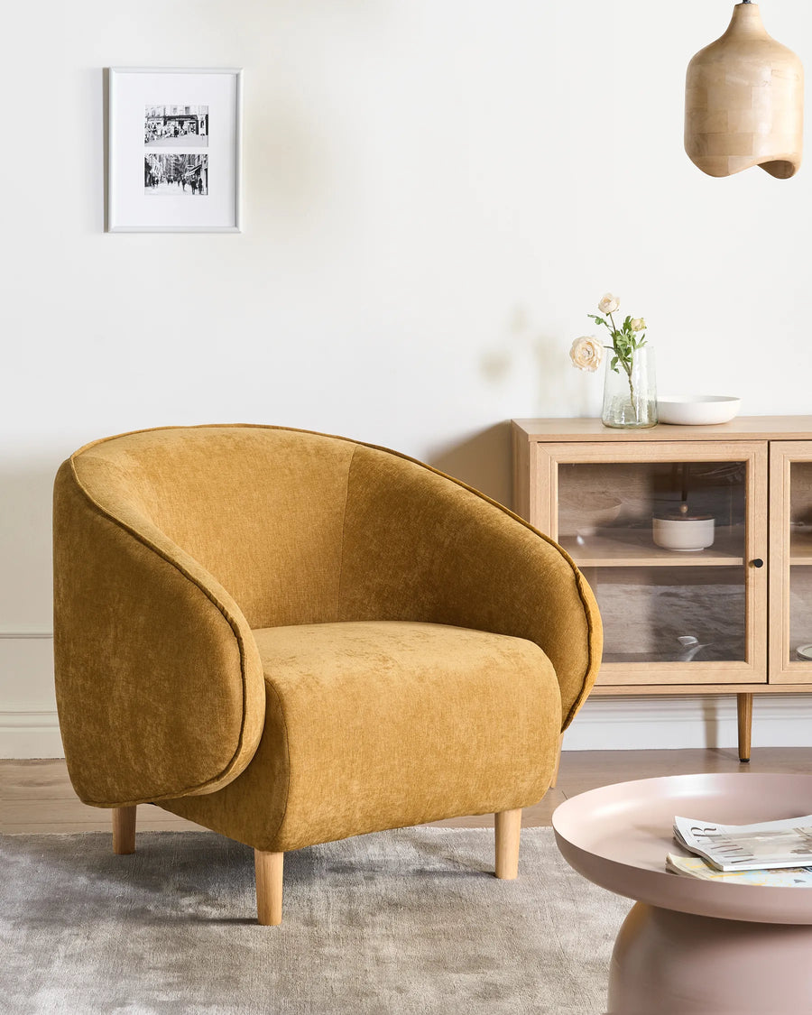 Mustard yellow armchair in a living room setting with a coffee table and cabinet.