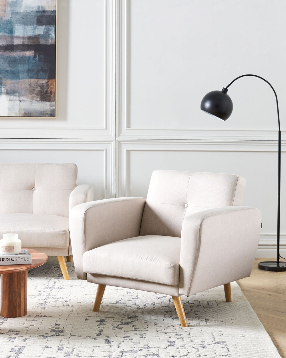 A beige upholstered armchair with a wide, padded seat and adjustable headrest, featuring button tufting and slanted wooden legs, positioned in a well-lit, modern living room setting.