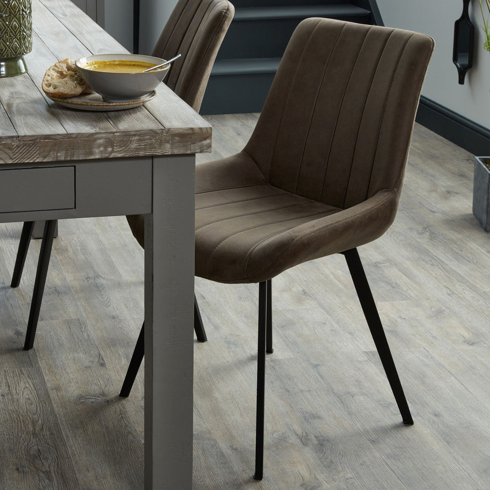 Dining table with a bowl of soup and bread, accompanied by a brown upholstered chair on a wooden floor.