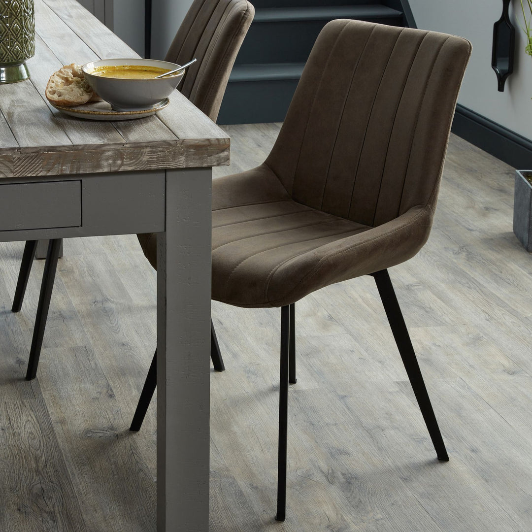 Dining table with a bowl of soup and bread, accompanied by a brown upholstered chair on a wooden floor.