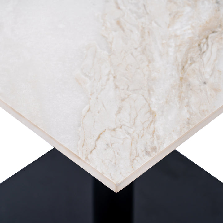 Close-up of a rectangular table corner with a white marble-look top featuring soft beige and cream veining, set against a black pedestal base on a white background.