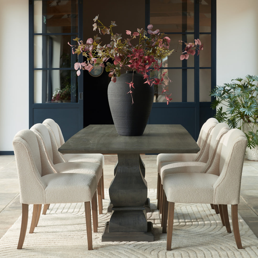 Dining room with a dark gray pedestal table and four chairs, featuring a vase with flowers.