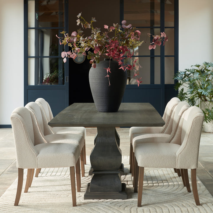 Dining room with a dark gray pedestal table and four chairs, featuring a vase with flowers.