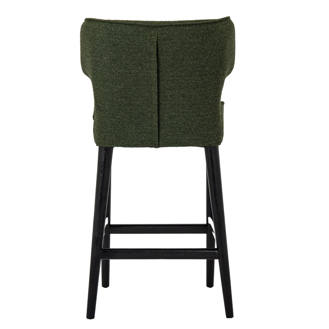 An upholstered bar stool with a textured dark green fabric seat and backrest, supported by four black wooden legs and a footrest.
