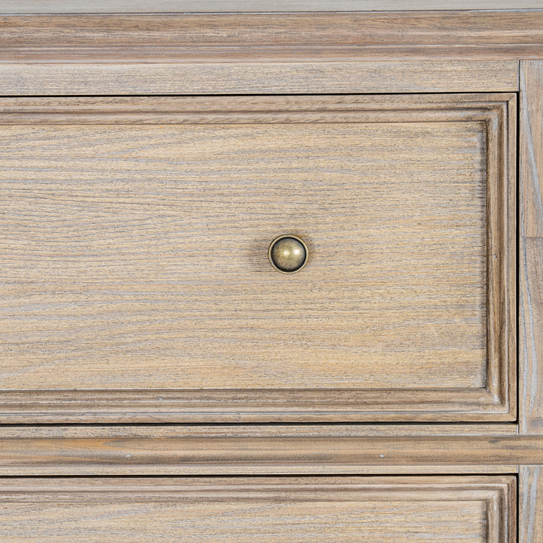 Close-up of a wooden furniture drawer front with a round brass pull knob, showing natural wood grain and raised panel detailing.