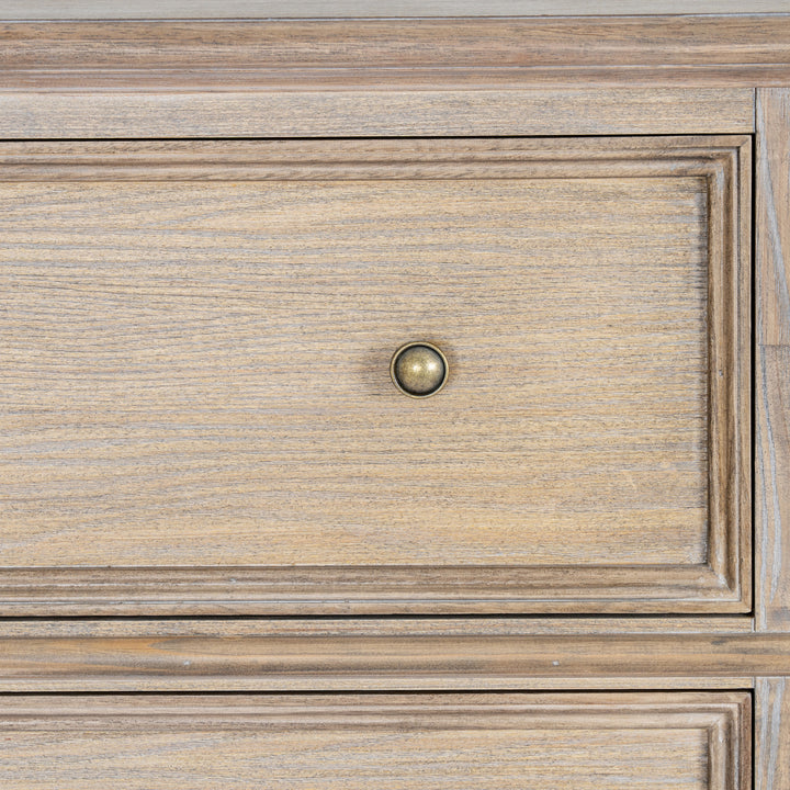 Close-up of a wooden furniture drawer front with a round brass pull knob, showing natural wood grain and raised panel detailing.