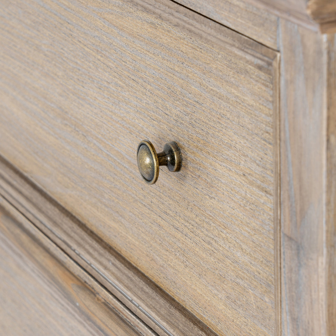 Close-up of a light oak wood cabinet drawer featuring a round antique brass knob.