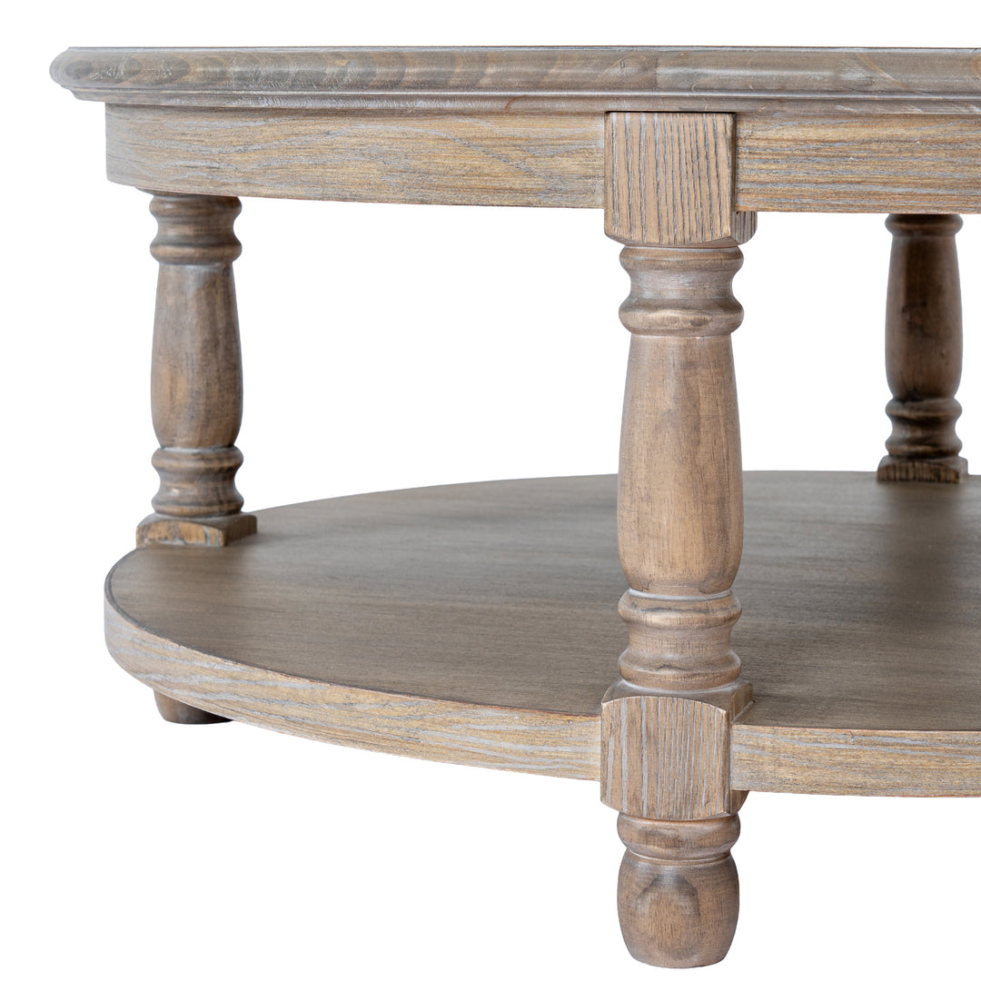 Close-up of a rustic round wooden coffee table with a distressed gray-brown finish, featuring a top surface, a lower shelf, and turned legs on a white background.