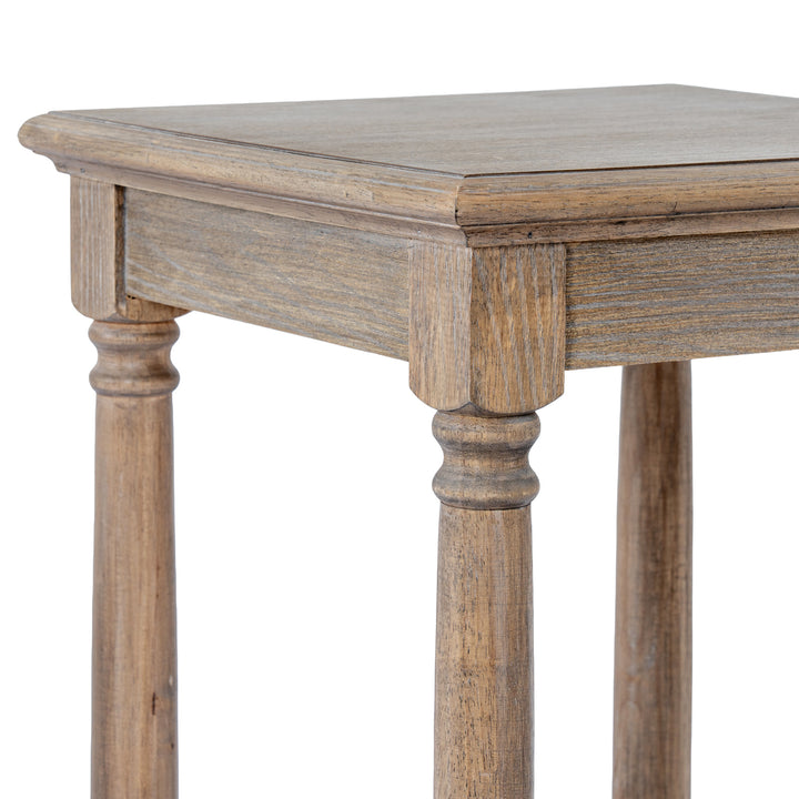 Close-up of a rustic wooden table corner showing the tabletop, apron, turned legs, and visible wood grain in a weathered brown finish against a white background.
