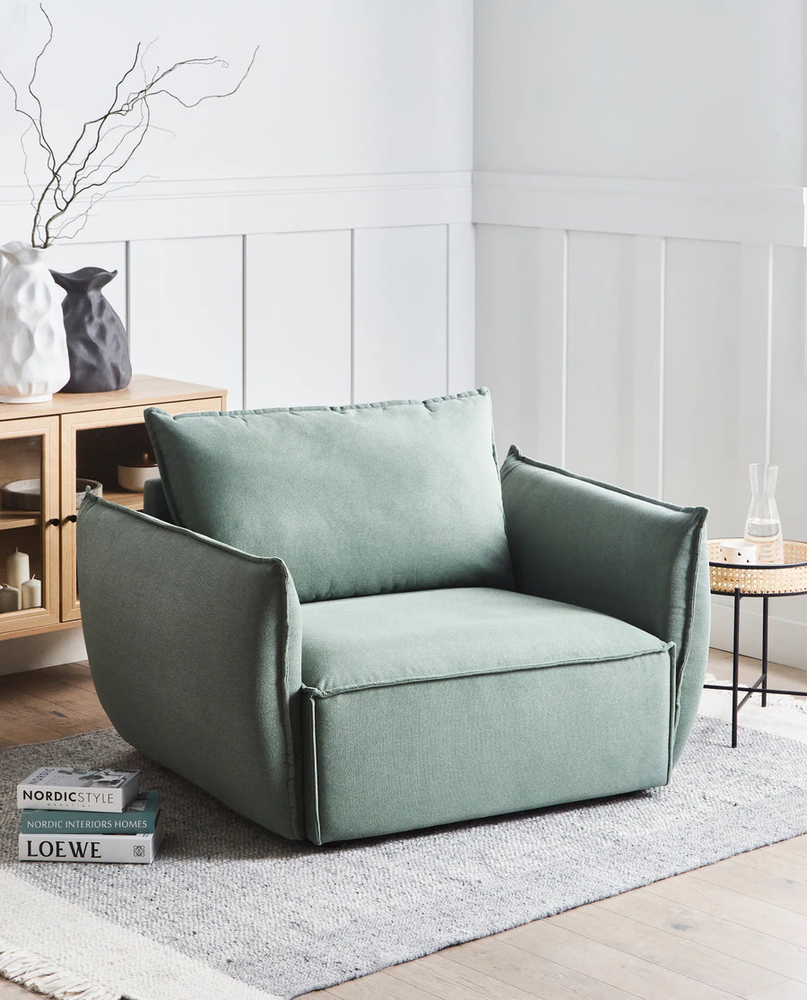 Green armchair in a modern living room setting with a light gray wall and wooden floor.