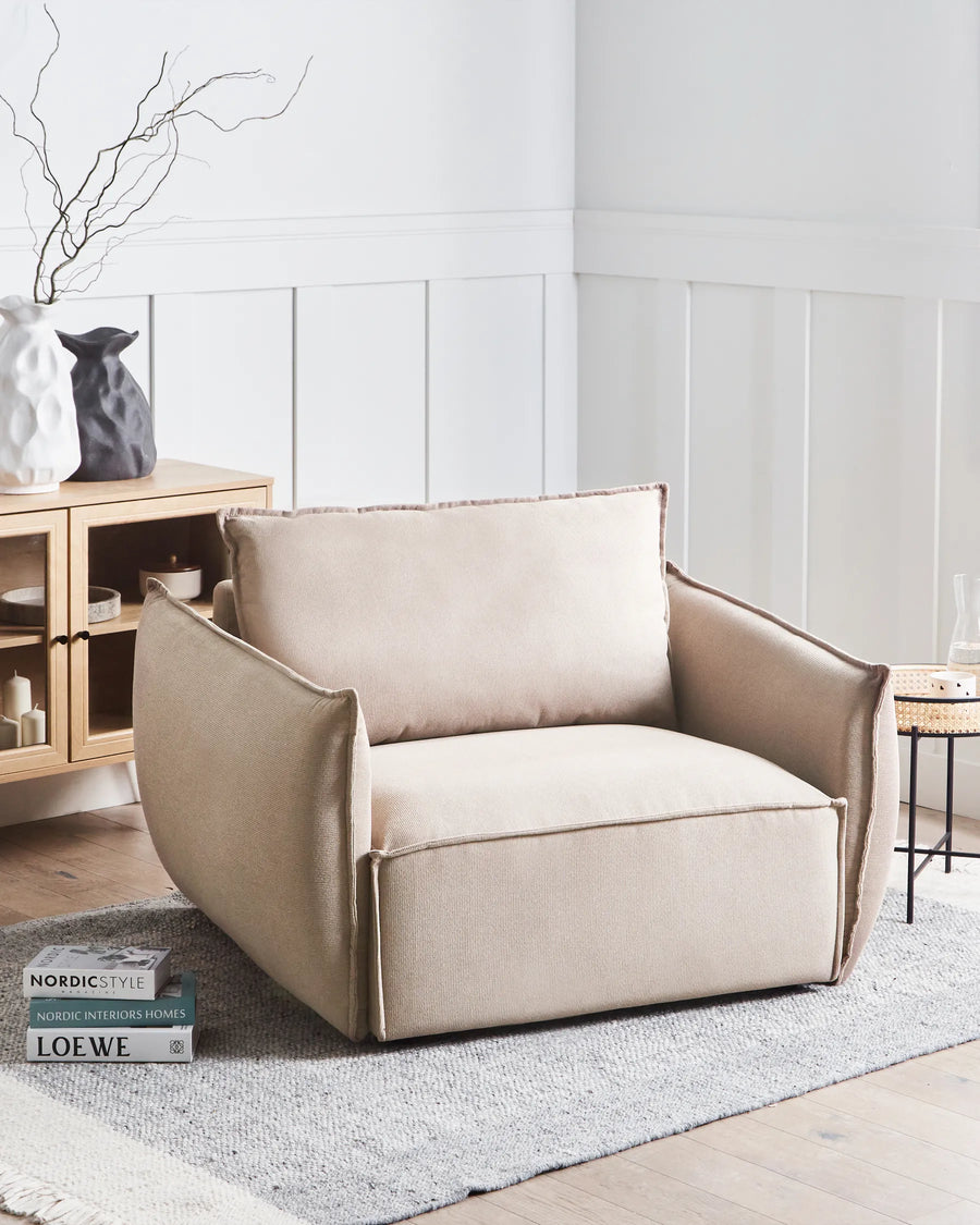 Beige armchair in a modern living room setting with a light gray wall and wooden floor.