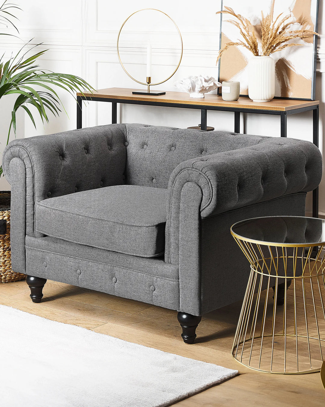 Gray tufted armchair in a room with a gold side table and decorative items.