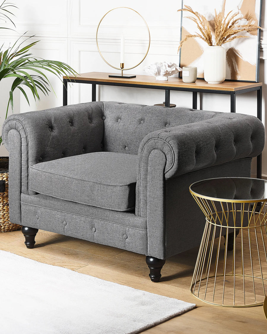 Gray tufted armchair in a room with a gold side table and decorative items.