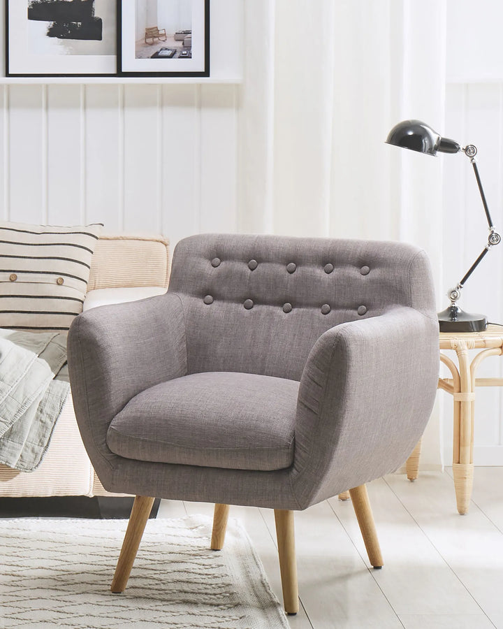 Gray armchair in a living room setting with a lamp and pillows.