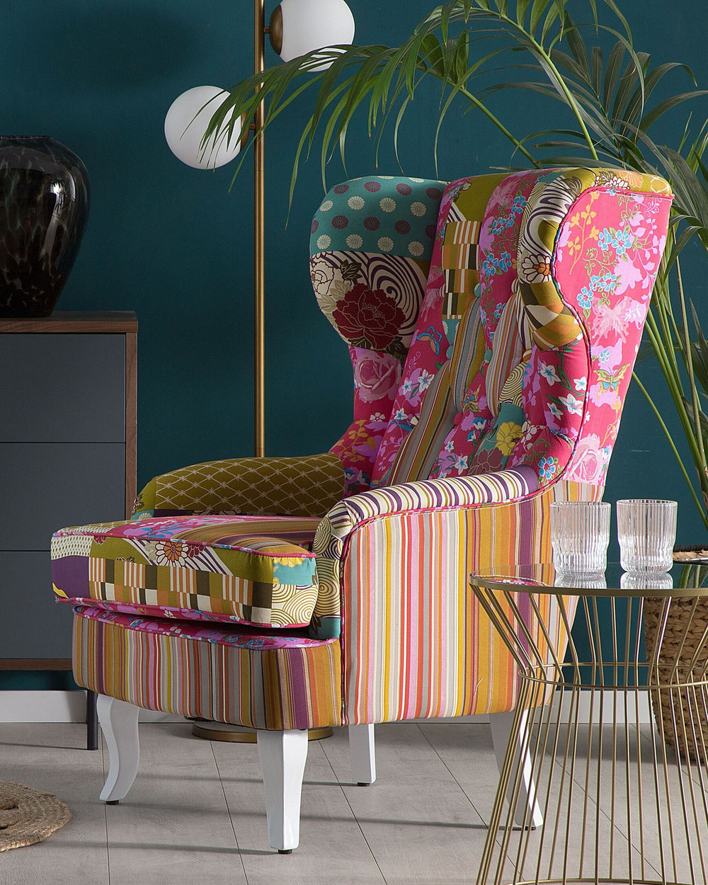 A vintage style upholstered armchair with a patchwork design featuring multiple colors including pink, white, yellow, and blue. The armchair has solid wooden legs and is positioned in a room with a dark wall and light flooring.
