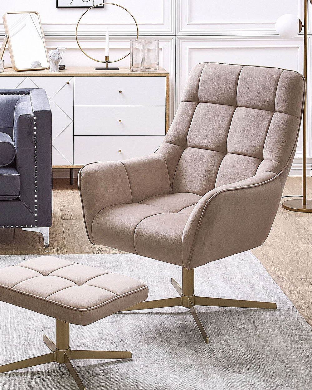 A beige velvet armchair with gold metal legs, accompanied by a matching footstool, set against a modern interior background.